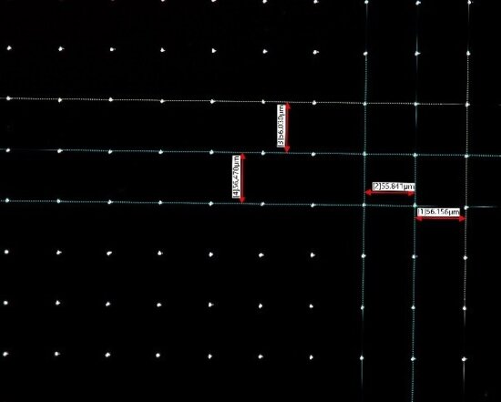 A grid of evenly spaced white dots on a black background with intersecting vertical and horizontal lines. Some lines are labeled with red and white measurement tags showing micrometer values.