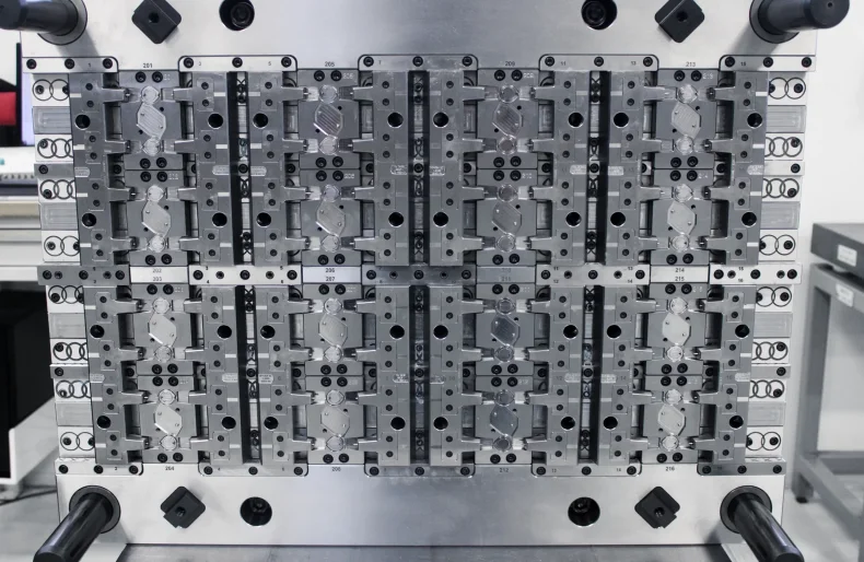 Close-up of a precision metal injection mold tool with multiple identical cavities arranged in a grid, used for manufacturing plastic or metal parts in an industrial setting.