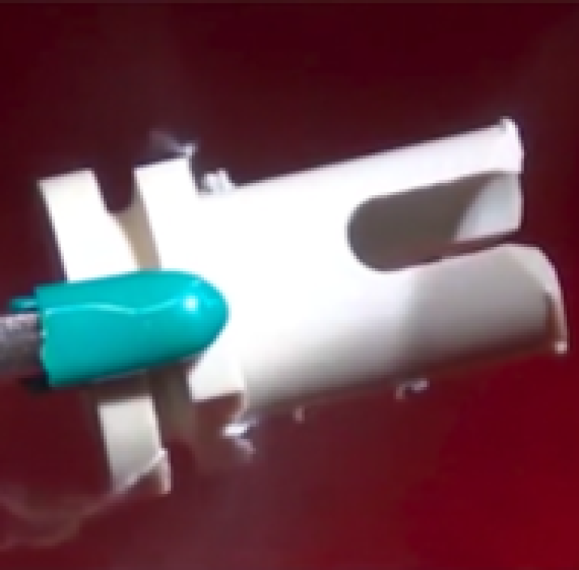 A close-up of a medical instrument with a teal-colored tip touching a white plastic component, set against a red background. Thin wisps of vapor or smoke are visible around the contact area.