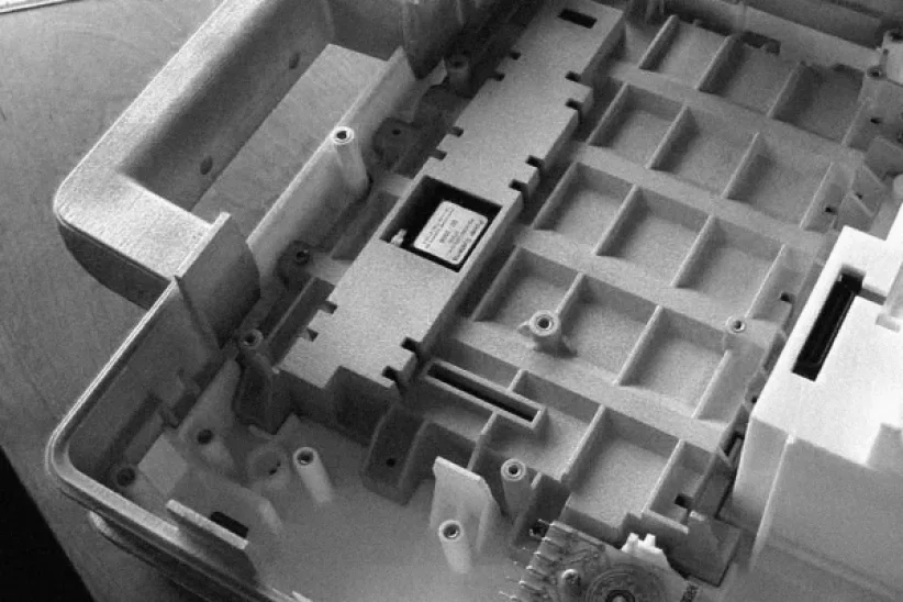 Close-up of the interior of an electronic device showing a rectangular chip installed on a gray plastic frame with multiple compartments and screws, viewed from above.