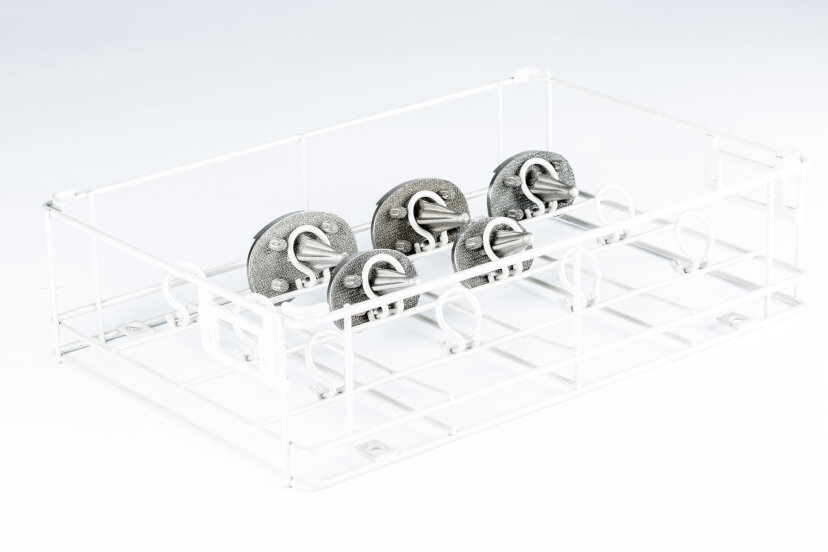 Ein weißes Metallgestell enthält vier runde, metallische Objekte, die gleichmäßig in einer Reihe angeordnet sind und an denen jeweils ein gedrehtes, mit einer Schleife versehenes Metallteil befestigt ist. Der Hintergrund ist einfarbig weiß.