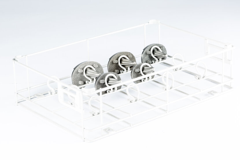 A white metal rack holds six circular metal objects with handles, arranged in two rows. The rack appears to be designed for organizing or storing these items. The background is plain and white.
