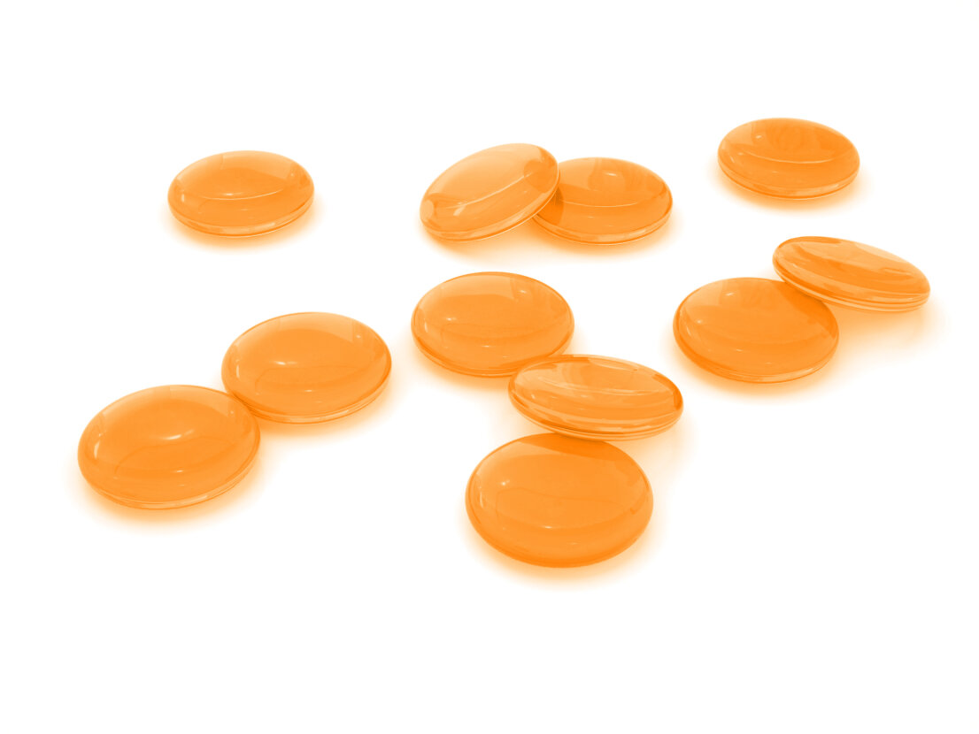 Zehn glänzende, runde, orangefarbene Tabletten oder Lutschtabletten sind auf einer weißen Fläche verstreut. Die Tabletten erscheinen glatt und glänzend und sind gleichmäßig in keinem bestimmten Muster angeordnet.