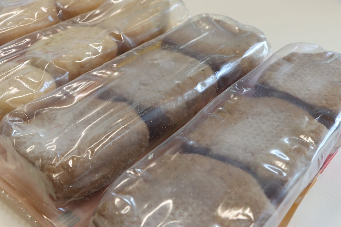Mehrere gefrorene Fischstücke sind in einer durchsichtigen Plastikverpackung vakuumverpackt und in Reihen auf einer hellen Fläche angeordnet.