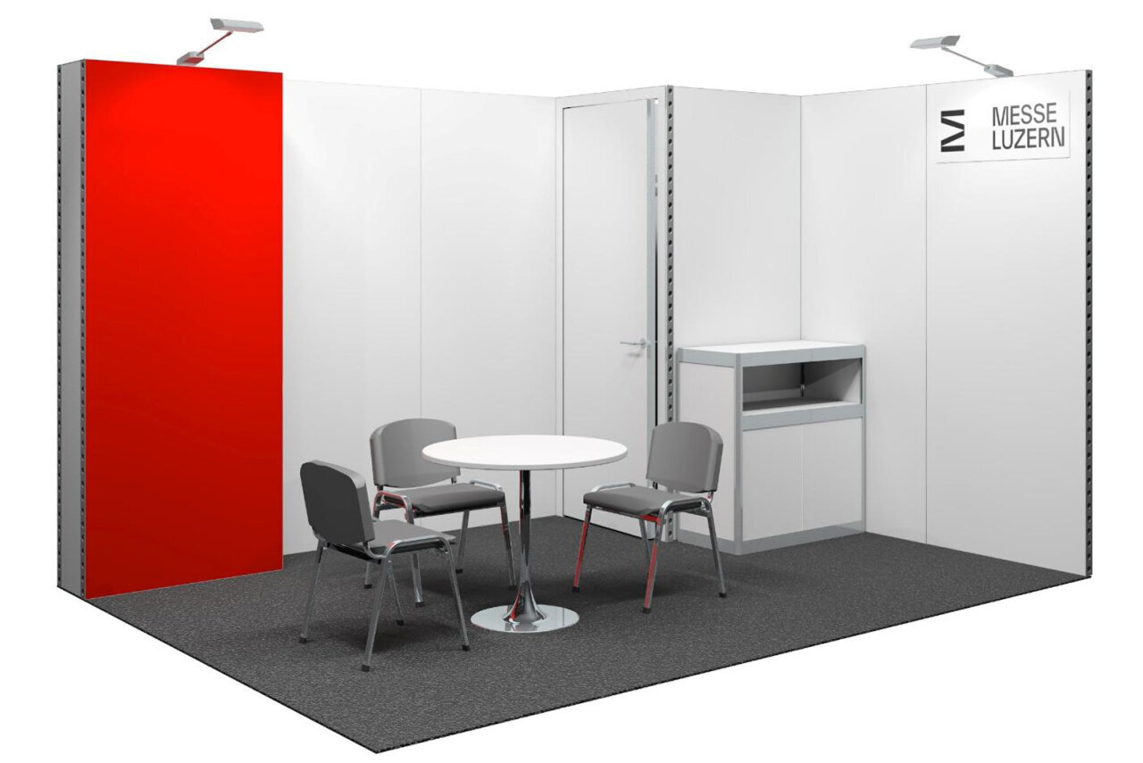 A simple trade show booth featuring a round table, four gray chairs, a white storage cabinet, white walls, a red wall, and a sign reading “Messe Luzern.” Ceiling lights illuminate the space.